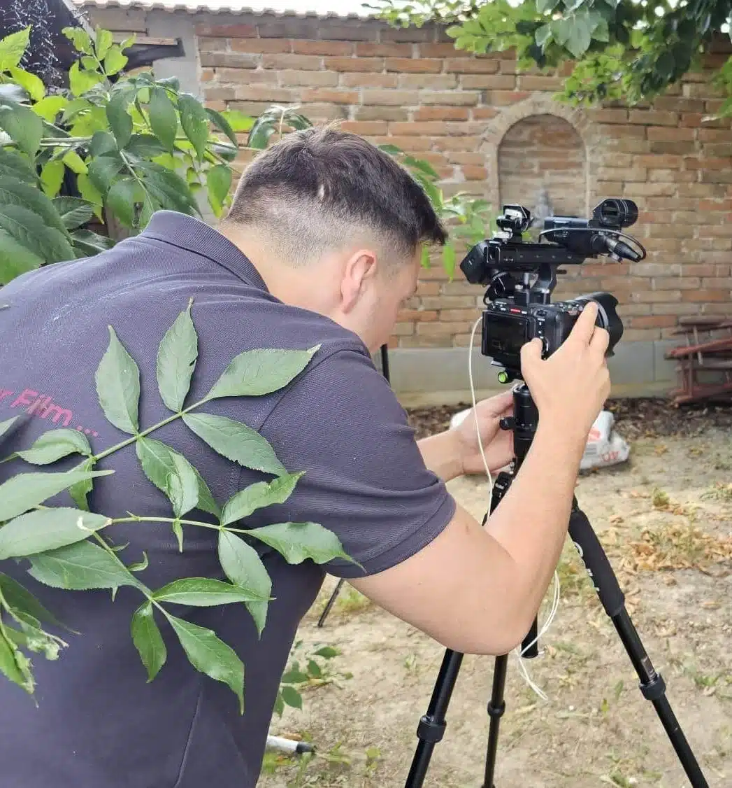 Person filmt Frau im Garten, die an einem Tisch sitzt. Videoaufnahme für einen Urban Film unter einem Baum.