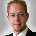 Eine Person in formeller Kleidung schaut freundlich in die Kamera.
