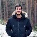 Eine Person in Winterjacke lächelt in einem verschneiten Wald, ideal für Imagevideos mit naturfreundlichem Kontext.