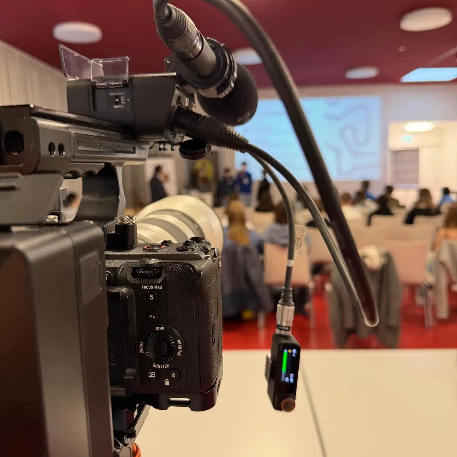 Kamera filmt eine Präsentation in einem modernen Konferenzraum mit Publikum im Hintergrund.