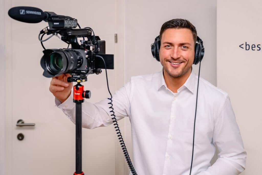 Person mit Kopfhörern bedient eine professionelle Videokamera, im Rahmen eines Filmprojekts in einem Büroraum.