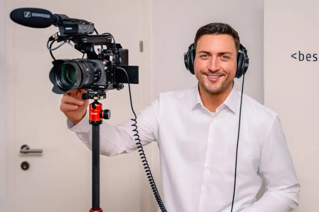 Person mit Kopfhörern bedient eine professionelle Videokamera, im Rahmen eines Filmprojekts in einem Büroraum.