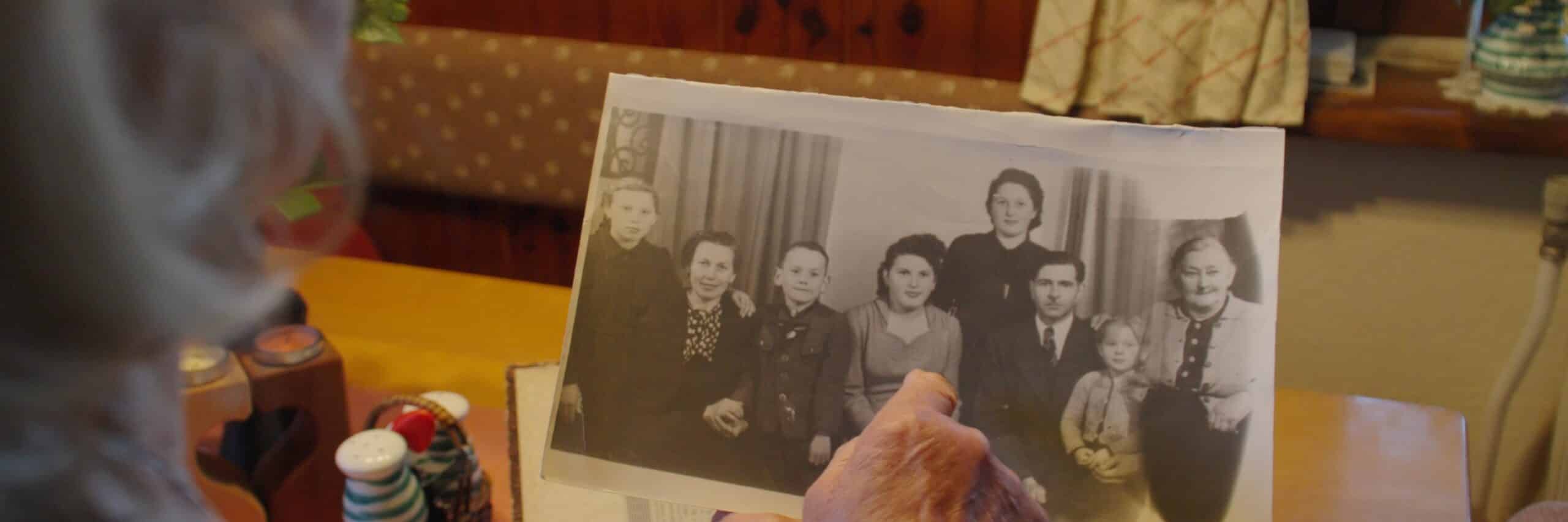 Eine Person hält ein altes Schwarz-Weiß-Foto von mehreren Menschen in einem gemütlichen Raum.
