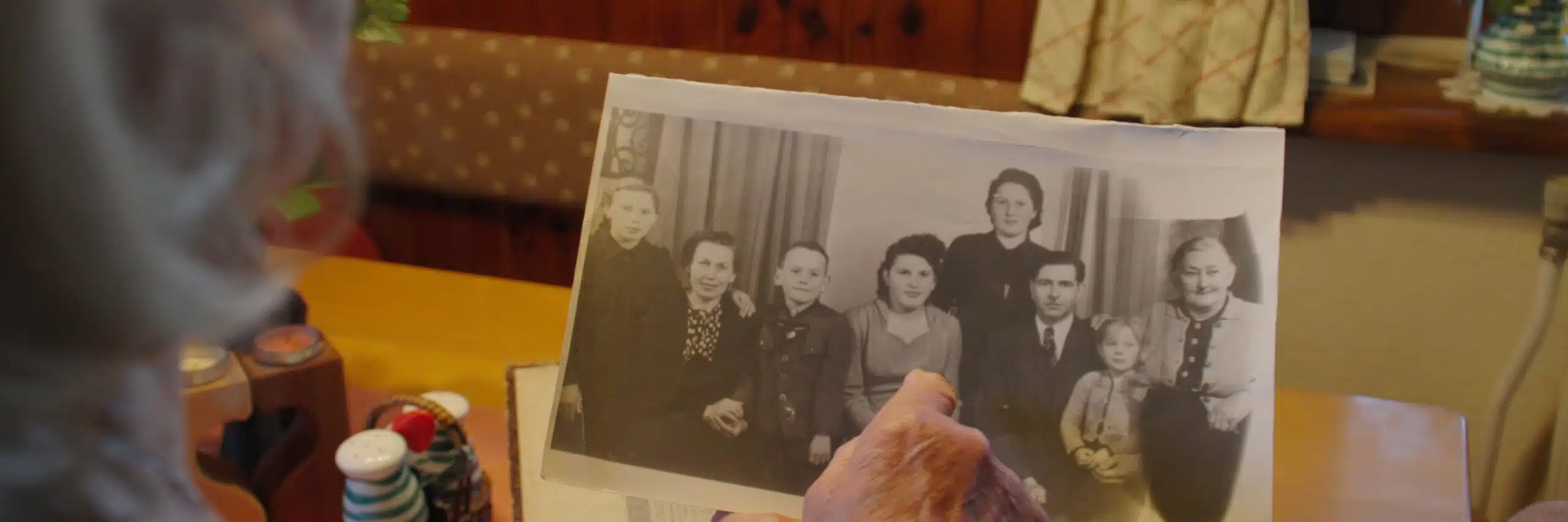 Eine Person hält ein altes Schwarz-Weiß-Foto von mehreren Menschen in einem gemütlichen Raum.