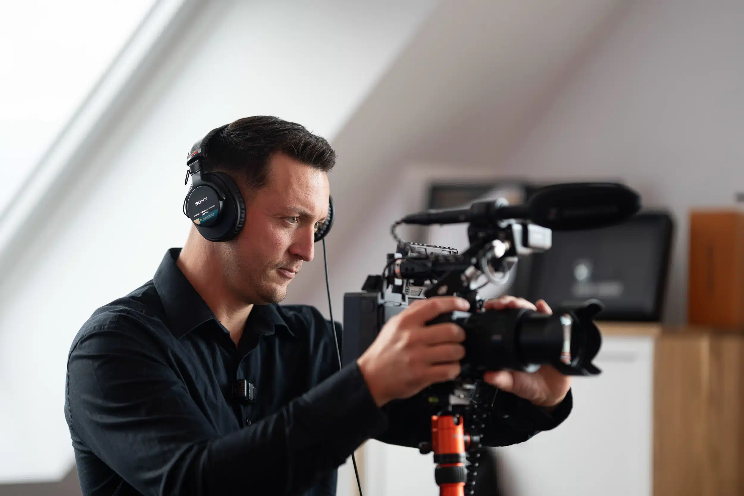 Person mit Kopfhörern bedient professionelle Filmkamera im Innenraum, konzentriert beim Videodreh für Image- oder Gemeindefilm.